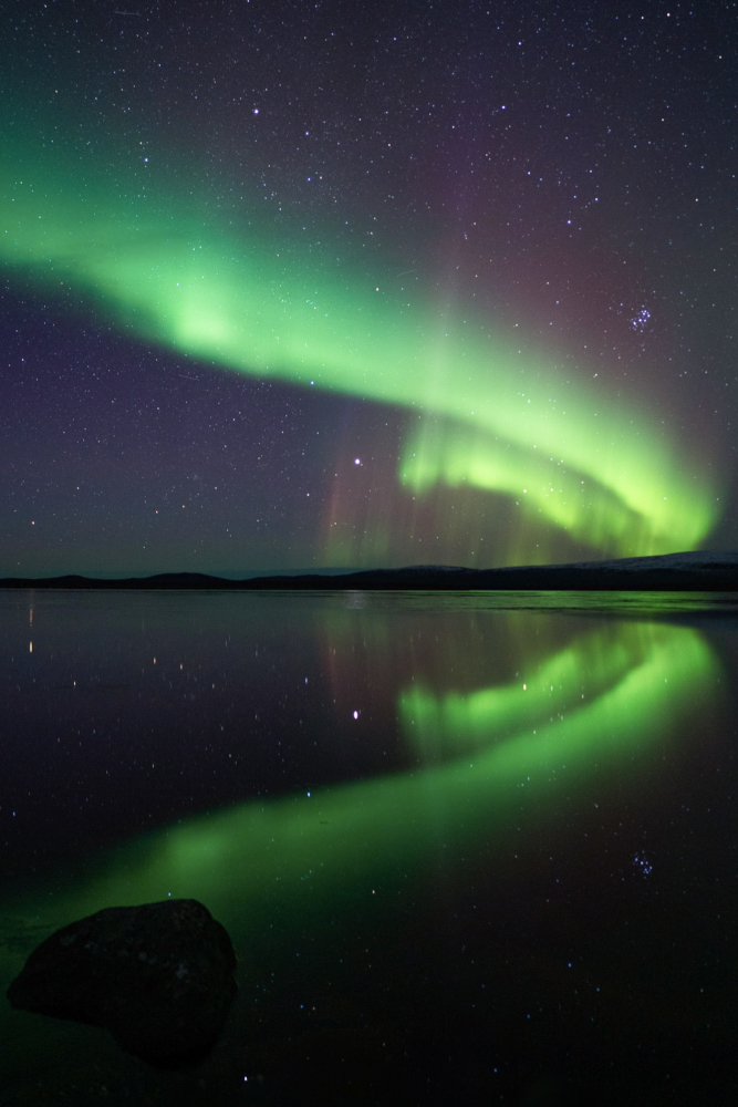 Aurora boreal en forma d'espiral verda reflectida sobre un llac glaçat a Nikkaluokta, Lapònia sueca.