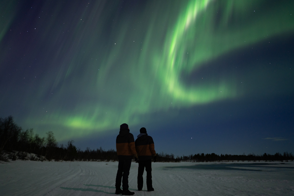 Dues persones observant una aurora boreal sobre el cel de la Lapònia sueca, a Kiruna.