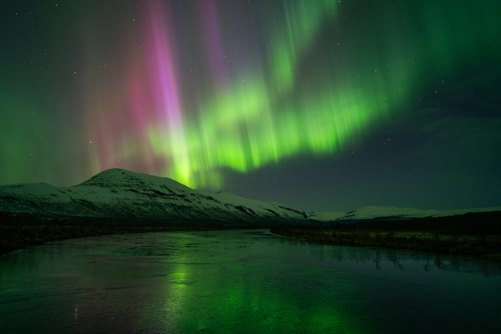 Aurora boreal brillant il·luminant muntanyes i llac glaçat a Lapònia sueca, a Nikkaluokta.