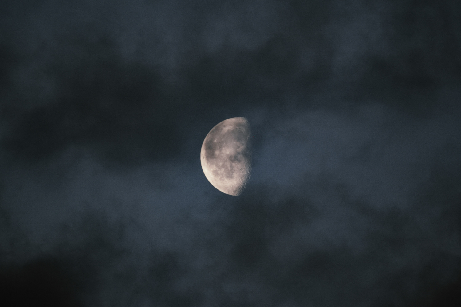 Lluna en quart minvant sortint entre els núvols en moviment, amb una llum suau i misteriosa que es filtra pel cel nocturn.