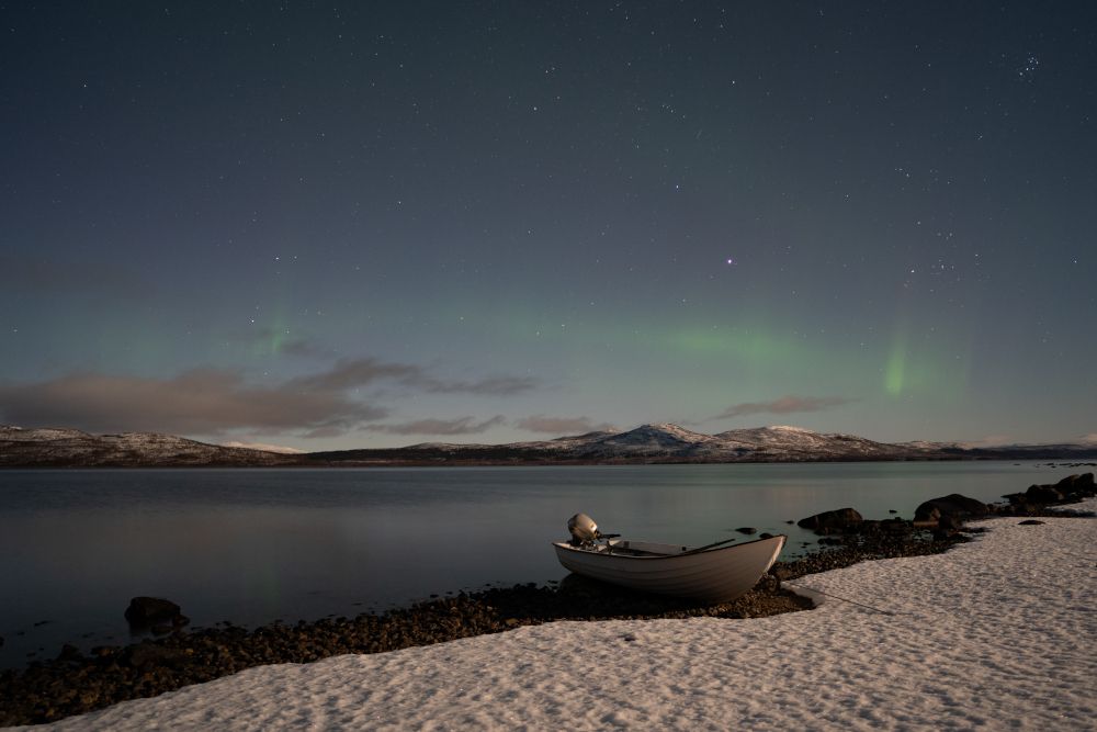 Paisatge àrtic amb barca, llac Torneträsk i aurora boreal suau de fons.